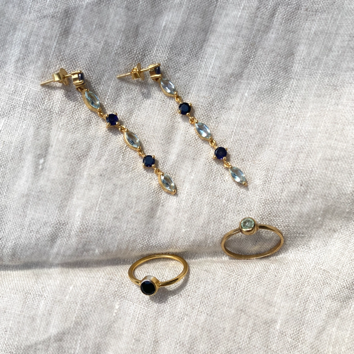 Een paar gouden oorbellen met blauwe en transparante edelstenen en twee gouden ringen met edelstenen.